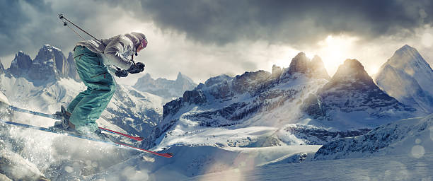 Eine weibliche Extremskifahrerin in einem mittleren Luftsprung beim Skifahren in der Höhe im Schnee. Die Handlung findet in einer generischen Bergkette statt, unter einem stürmischen Abendhimmel mit einem dramatischen Sonnenuntergang. Das Bild enthält absichtliches Bokeh und Spray. Der Skifahrer ist in generischer Skiausrüstung und markenlosen Skiern gekleidet.