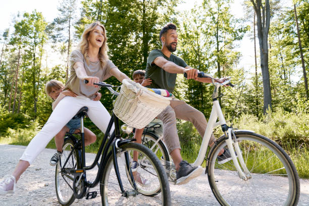 exuberant family riding bicycles in the forest - fietsen stockfoto's en -beelden