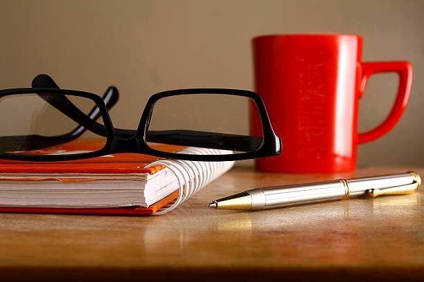 Eyeglasses, coffee mug, notebook and a pen stock photo