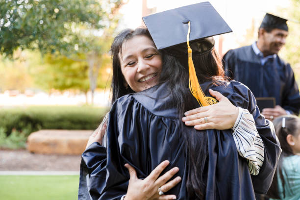 Eyes closed, mother embraces unrecognizable daughter in cap and gown Outside after the graduation, the mid adult mother closes her eyes as she joyfully embraces her unrecognizable daughter. universities stock pictures, royalty-free photos & images