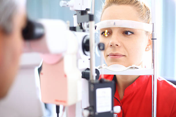 Eyesight exam. Closeup of late 20's  blond woman visiting optician. She placed her head into phoropter machine while senior male doctor is examining her eyesight. The woman has brown eyes and wearing red t-shirt. human eye stock pictures, royalty-free photos & images