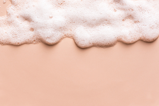 Face cleansing mousse sample. White cleanser foam bubbles on nude background, copy space. Soap, shower gel, shampoo foam texture border.