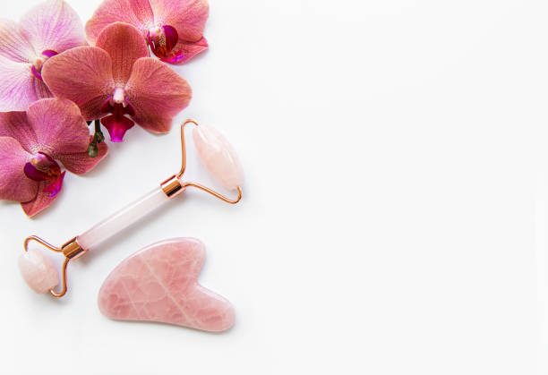 Face massage jade rollers on white background Face massage jade rollers and orchid flowers   on white background gua sha tools stock pictures, royalty-free photos & images