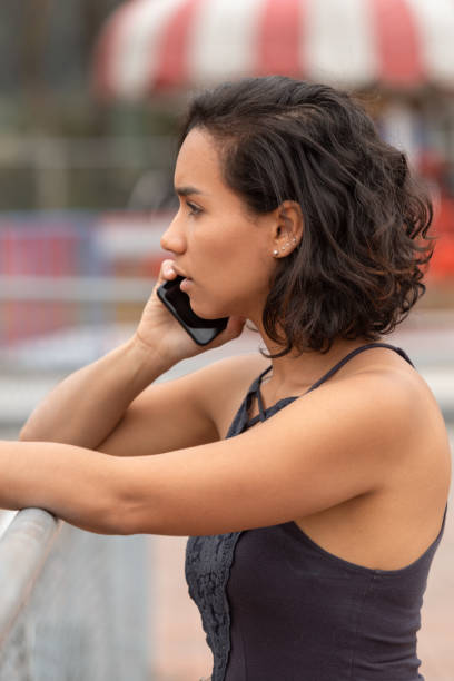 face of young brunette latin woman with short hair and curls in profile, talking on the phone face of young brunette latin woman with short hair and curls in profile, talking on the phone, she has a light tank top, natural light outside south american woman stock pictures, royalty-free photos & images