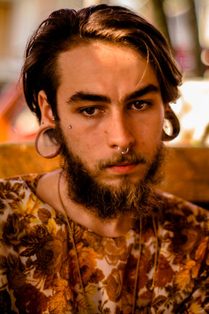 Retrato do rosto de um homem jovem, com barba e cabelo castanho, brinco piercing e exóticas nariz captou ao entardecer