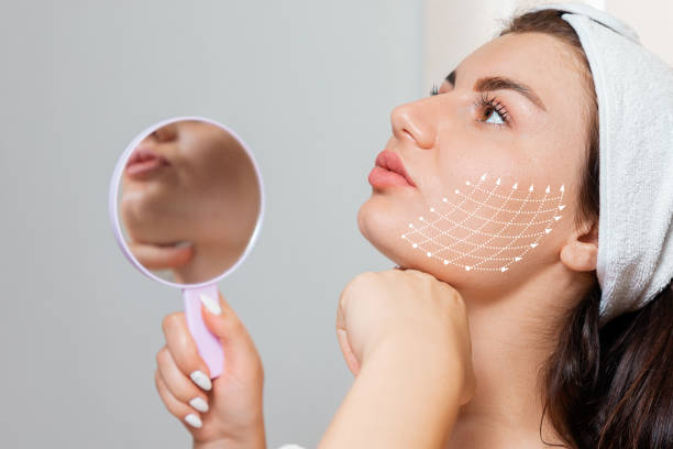 Facial lifting thread. Woman holding a mirror and show her cheak with arrows skin, contouring using mesothreads. Concept of plastic surgery Facial lifting thread. Woman holding a mirror and show her cheak with arrows skin, contouring using mesothreads. Concept of plastic surgery. thread lifting stock pictures, royalty-free photos & images