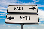 istock Fact versus myth road sign with two arrows on blue sky background. White two street sign with arrows on metal pole. Two way road sign with text. 1320686088