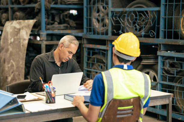 Factory manager looking at the paper with young engineer sitting front for call for blaming or consider and interview job apply or solving working problem report situation at factory work stock photo