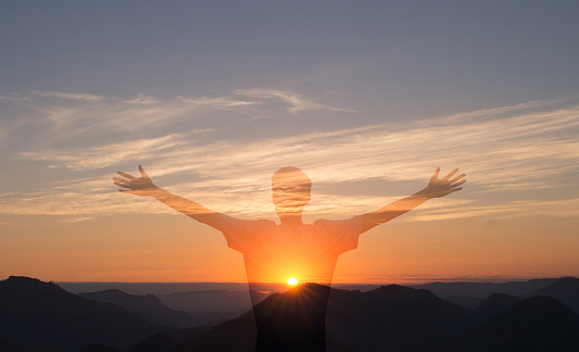 Man with arms raised with sunset in the mountains in the background. Person worshiping or thanking God. Success and happiness concept.