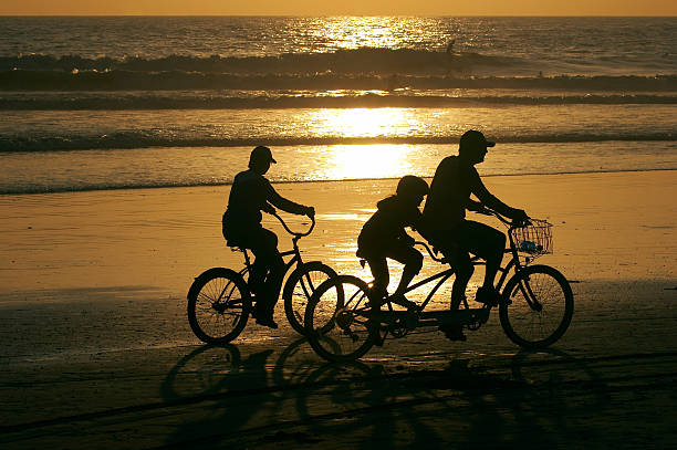 Parents and a child riding bikes along the beach at sunset.