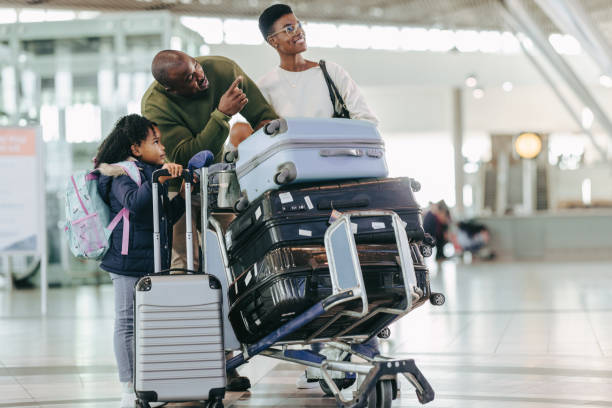 Family at airport with their luggage on trolley Dad showing the flight information board to his daughter standing at airport terminal. Young family and waiting for flight at airport with their luggage on trolley. luggage cart stock pictures, royalty-free photos & images