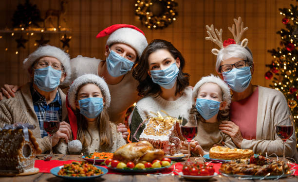 family celebrating Christmas Merry Christmas! Happy family are having dinner at home. Celebration holiday and togetherness near tree. People are wearing facemasks. dinner photos stock pictures, royalty-free photos & images