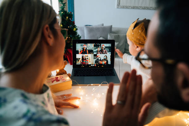 Family celebrating Christmas with their relatives respecting social distancing. They are doing a video call using a laptop to celebrate together. New normal during Coronavirus Covid-19 pandemic concept.