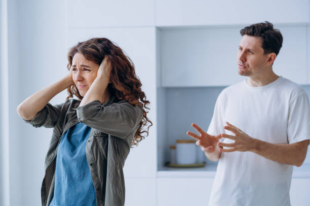 Family conflict, the husband yells at his wife standing at the window with her ears closed stock photo