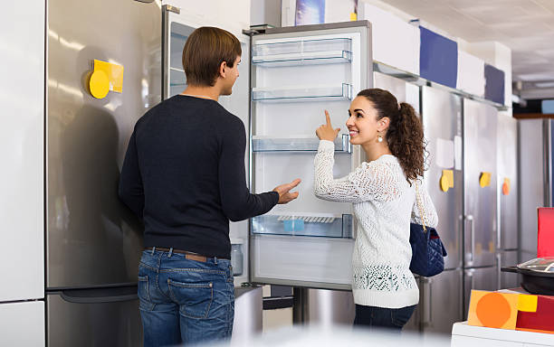family couple choosing new refrigerator in hypermarket Middle class russian family couple choosing new refrigerator in hypermarket appliance stock pictures, royalty-free photos & images
