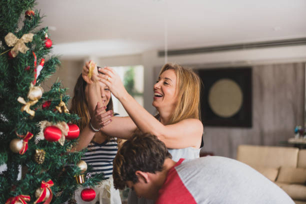familie decoranting de kerstboom thuis - vrouw kerstboom versieren stockfoto's en -beelden