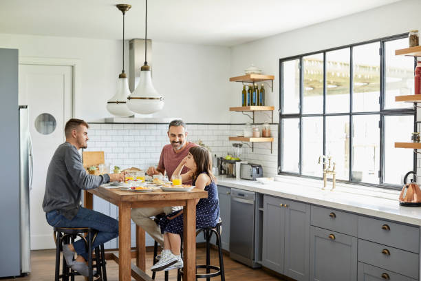 Family eating breakfast in kitchen at home Full length of family eating breakfast at table in kitchen. Homosexual fathers are sitting with daughter. They are in casuals at home. gay person stock pictures, royalty-free photos & images