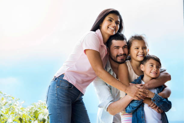 Family embraced in the garden Loving family, with dad and mom hugging their beautiful children in the garden of their house, while they look at the front and smile happily colombian ethnicity stock pictures, royalty-free photos & images