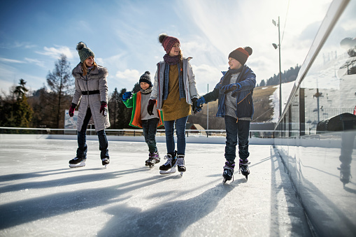 Mother and three kids spending time on ice-skating rink. \nNikon D850