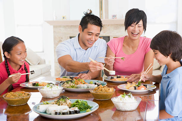 Family Enjoying Meal Together Family Enjoying Meal Together Smiling And Laughing asian family eating together stock pictures, royalty-free photos & images