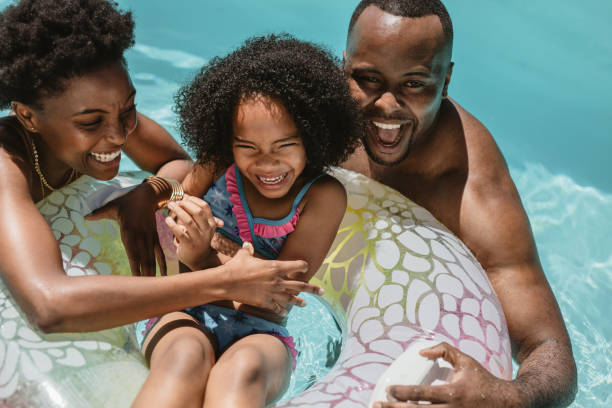 Family enjoying summer holidays in pool Man and woman playing with their daughter on inflatable ring in swimming pool. Family of three enjoying summer holidays in swimming pool. swimming pool photos stock pictures, royalty-free photos & images