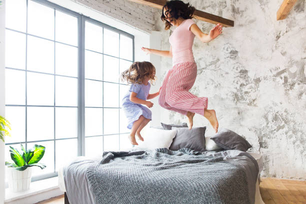 Family fun. Mother and daughter jumping on the bed stock photo