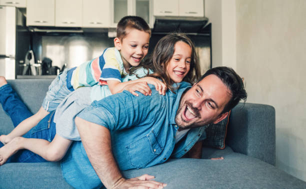 Family having fun at home. Young father playing with his two cute children on the sofa at home. fathers day stock pictures, royalty-free photos & images