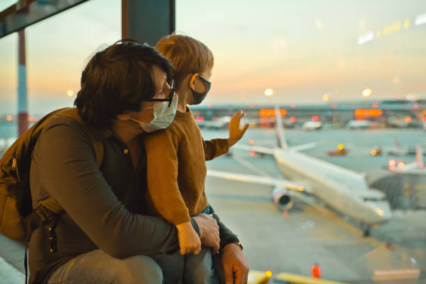 Family in protective face masks in airport during COVID-19 pandemic Father and son traveling by plane tourism stock pictures, royalty-free photos & images