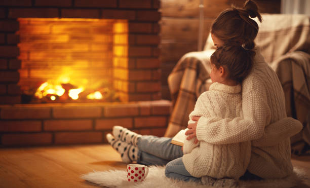 abbracci madre e figlio di famiglia e caldo la sera d'inverno con camino - riscaldamento foto e immagini stock