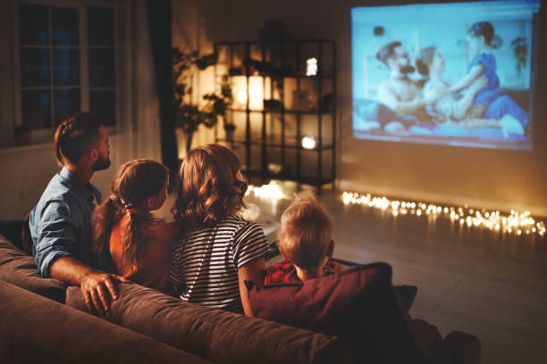 family mother father and children watching projector, TV, movies with popcorn in   evening   at home stock photo