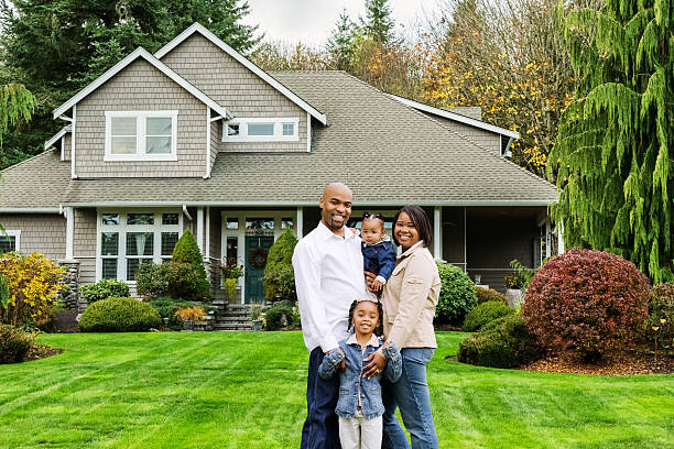 Family of Four at Home in Front Yard Portrait of a happy young African American family standing in front of their American suburban home. front yard stock pictures, royalty-free photos & images