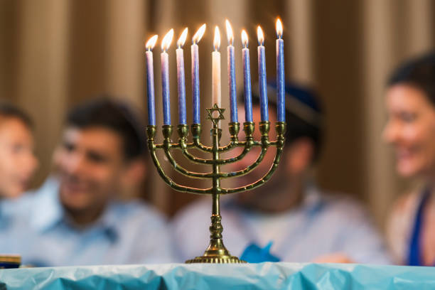 A jewish family of four sitting around a table talking, out of focus in the background. The younger boy is 7 years old and his brother is 13. The focus is on the menorah in the foreground
