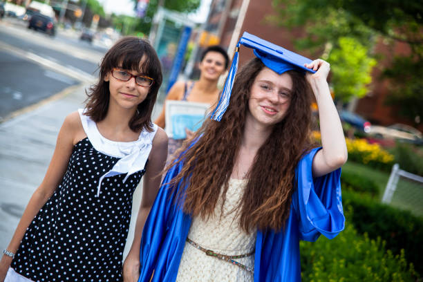Family of graduated middle-school student - her mother, and sister - is walking on the street in Queens, New York, USA. Focus on the girls, with the mother blurred in the backdrop. stock photo