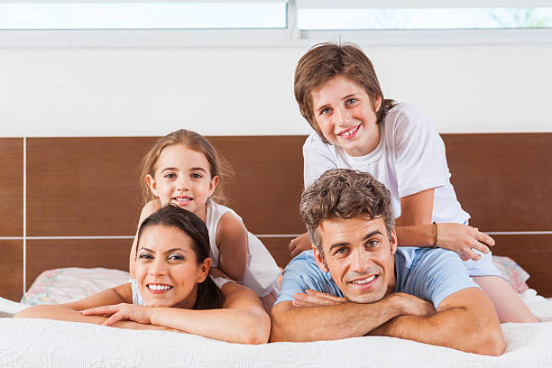 Happy family lying bed bedroom, couple smile with children