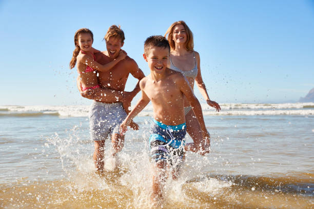 Family On Summer Beach Vacation Run Out Of Sea Towards Camera  little girls in bathing suits stock pictures, royalty-free photos & images