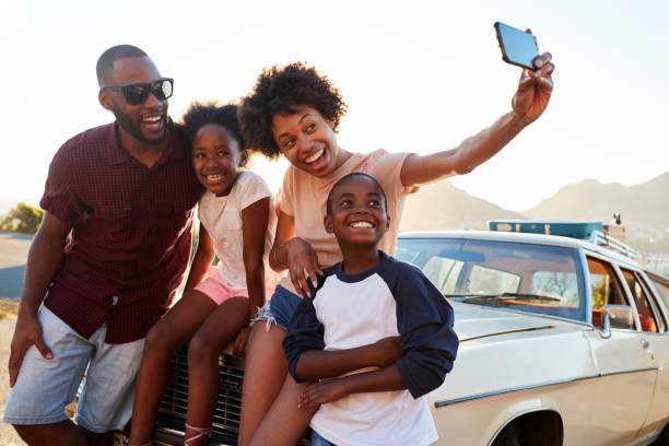 family posing for selfie next to car packed for road trip - family car imagens e fotografias de stock