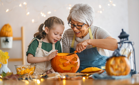 Happy family preparing for Halloween. Grandmother and granddaughter carving pumpkins at home.
