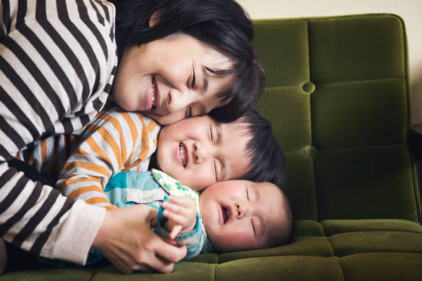 Family relaxed at home Japanese older brother hugging his younger sister. And Japanese mother hugging them together on sofa. baby human age photos stock pictures, royalty-free photos & images