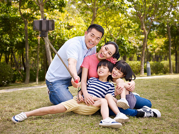 family selfie happy asian family with two children taking a outdoor selfie with selfie stick outdoors in a city park. child korea little girls korean ethnicity stock pictures, royalty-free photos & images
