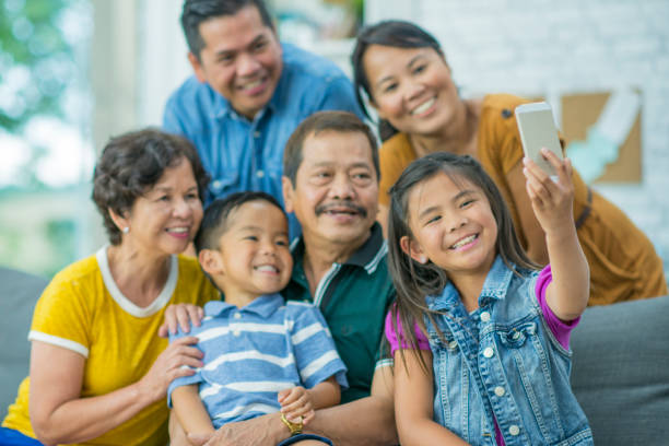 Family Selfie An Asian family is indoors in a living room. They are wearing casual clothing. They are taking a selfie together while sitting on a couch. filipino family stock pictures, royalty-free photos & images