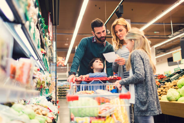 Family shopping in supermarket Cheerful family with two children shopping vegetables in supermarket. Holding shopping list and looking for groceries shopping list stock pictures, royalty-free photos & images
