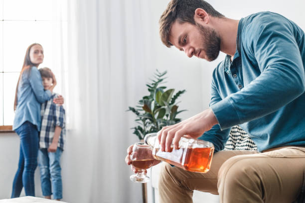 Family social problems father alcoholic concept man pouring whiskey Mother father and son social problems alcoholism man pouring whiskey into glass while wife with kid standing near window scared alcohol abuse stock pictures, royalty-free photos & images