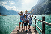 Family enjoying vacations in Italy. Father and kids are standing on a pier in Riva del Garda and cheering to the camera. Behind them there is magnificent view of Lake Garda surrounded by the Alps.
Nikon D850