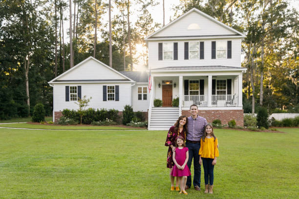 Family standing outside front of new construction white siding farmhouse in the suburbs stock photo