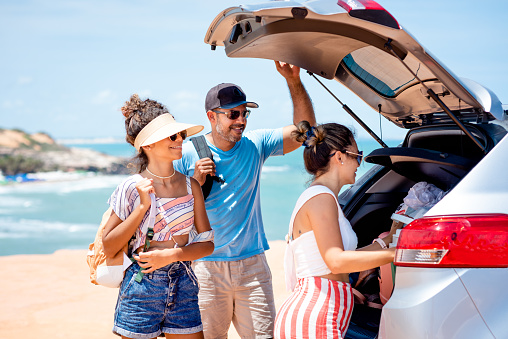 Parents and their teenager daughter unpacking car at beach during a roadtrip to the cost
