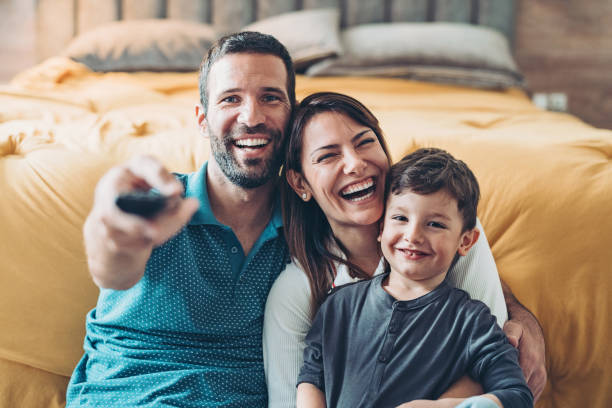 Family watching television together Two parents and a little boy with a TV remote control in the bedroom television industry stock pictures, royalty-free photos & images