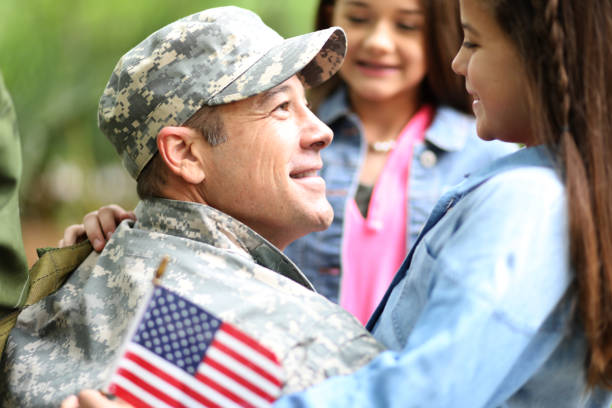 Family welcomes home USA army soldier. Family welcomes home a USA army soldier.  The children excitedly hug father holding American flags. soldiers returning home stock pictures, royalty-free photos & images