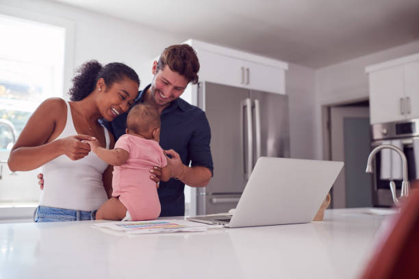 familie mit baby-tochter in der küche mit laptop auf theke - beide elternteile stock-fotos und bilder