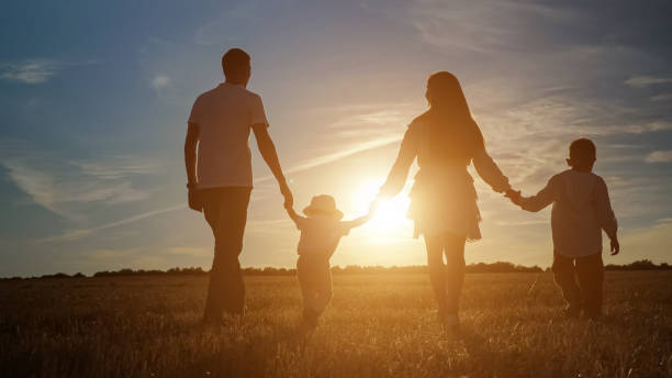 Family with children walks along fields at back setting sun stock photo