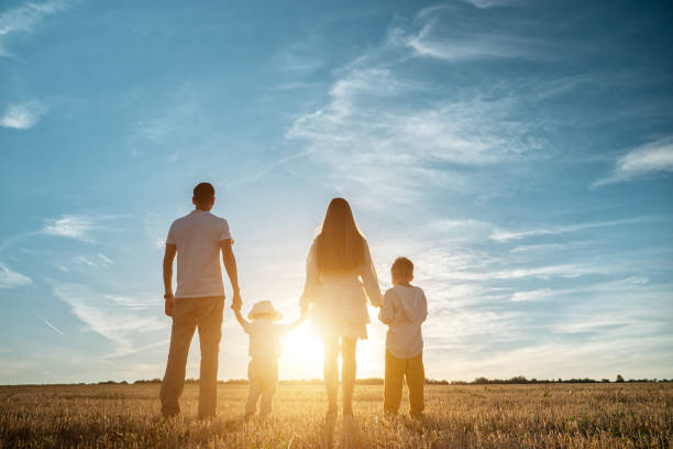 Family with children walks along fields at back setting sun stock photo